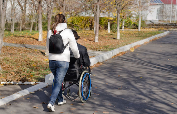 A woman pushing a man in a wheelchair along a tree-lined path